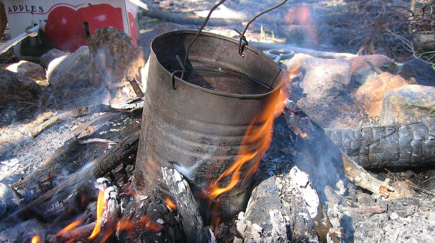 A blackened billy can heating among glowing coals and burning wood