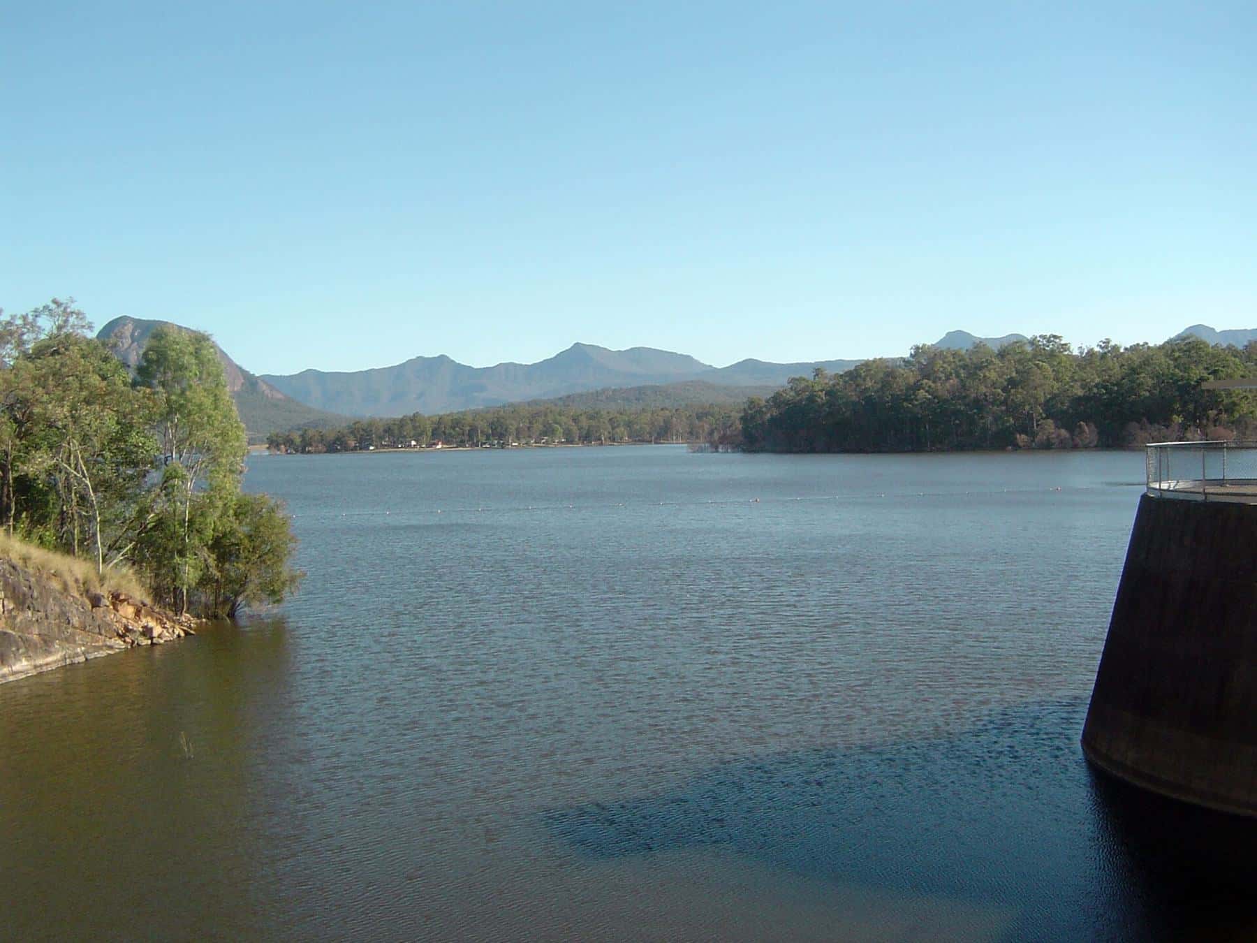 The calm blue water of Lake Moogerah with forested hills and the peaks of the Scenic Rim behind