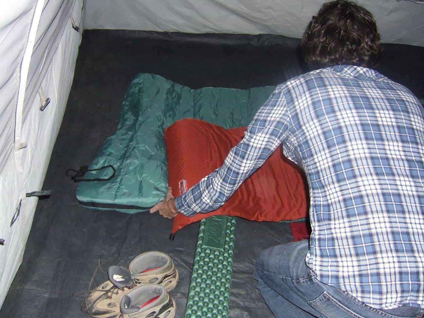 A camper kneeling inside a tent arranging a red sleeping bag on top of a sleeping pad