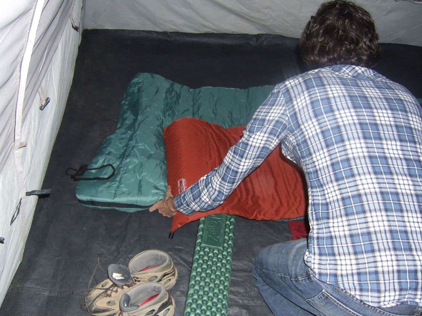 A camper kneeling inside a tent arranging a red sleeping bag on top of a sleeping pad